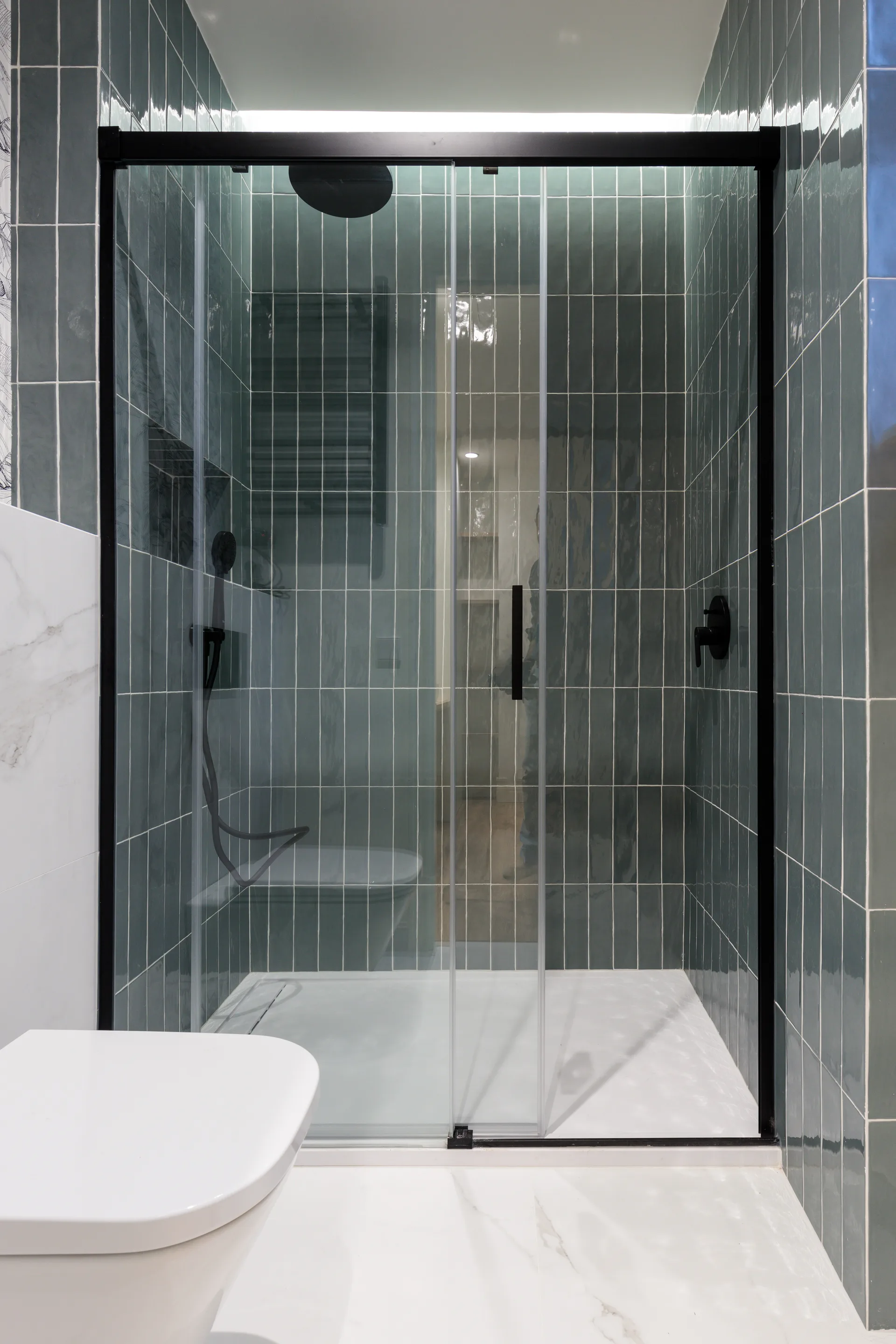 Reforma de baño moderno con mampara corredera negra y azulejo azul gris en Madrid